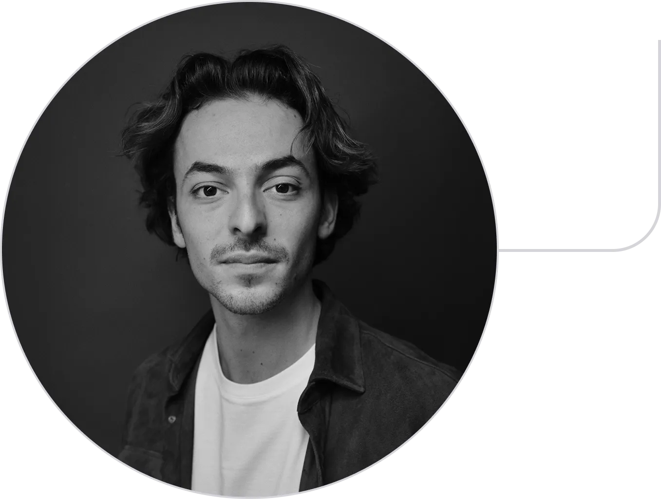 Black and white headshot of a young man with wavy hair, light stubble, wearing a white shirt and jacket.